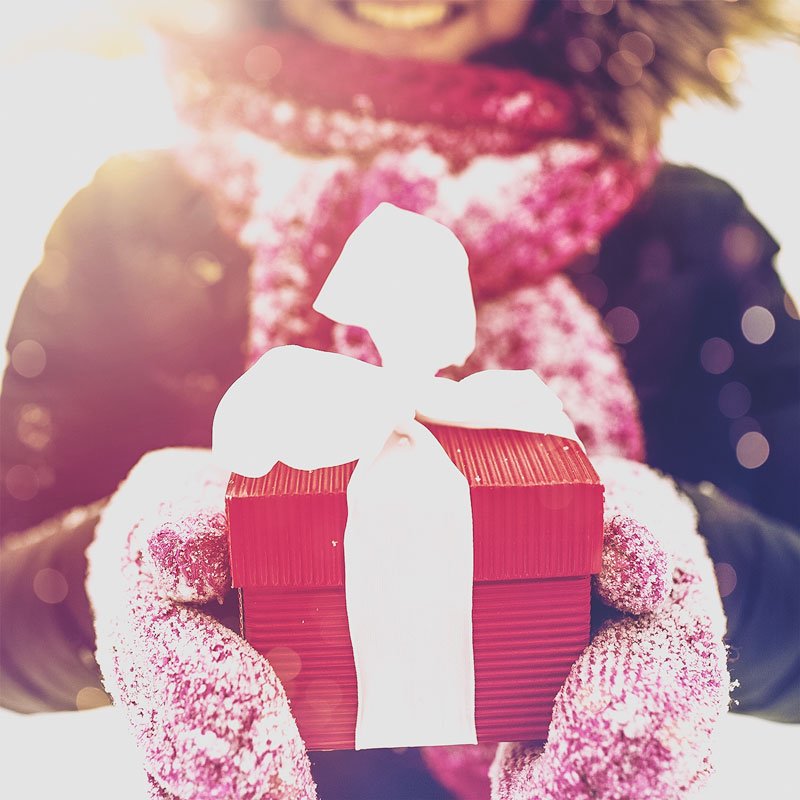 Cerca de una mujer sosteniendo una caja de regalo roja con una cinta blanca.